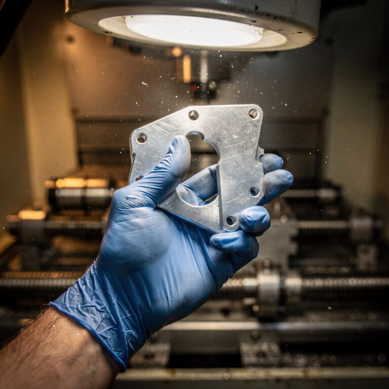 Machinist inspecting a freshly CNC-machined aluminum aerospace bracket under a factory inspection lamp