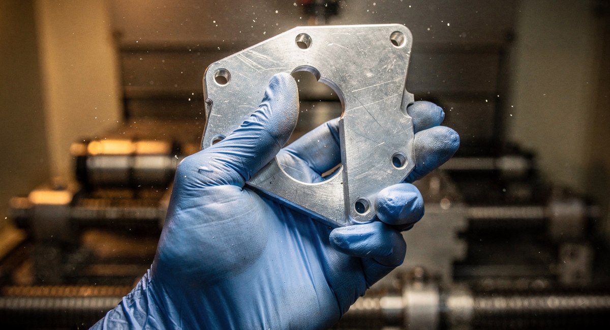 Machinist inspecting a freshly CNC-machined aluminum aerospace bracket under a factory inspection lamp
