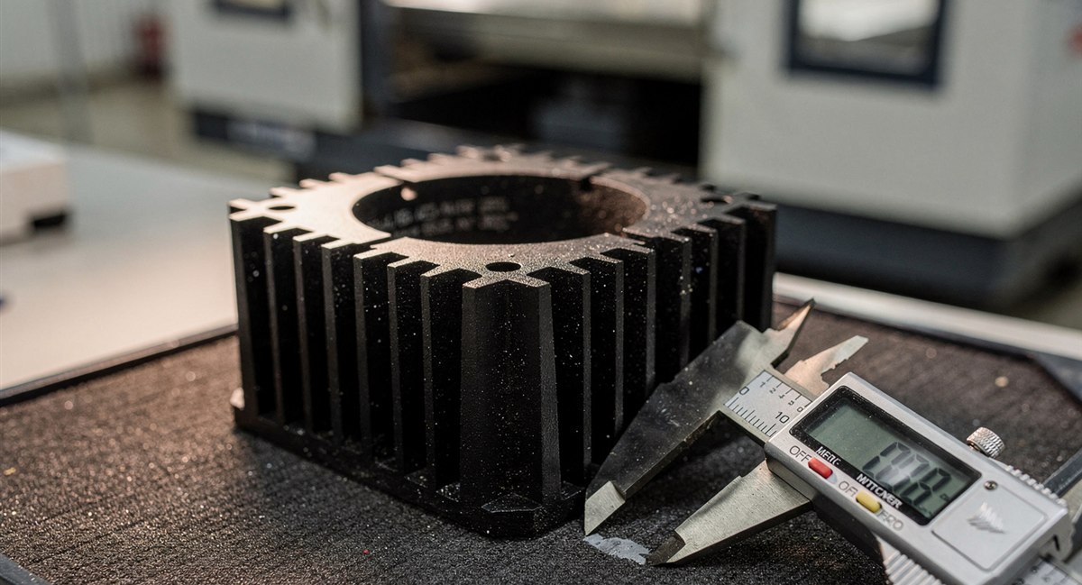 Matte black anodized aluminum LED heat-sink housing on an inspection tray with a digital caliper